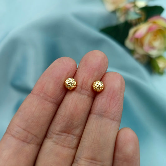 Aretes de bola dorada facetada, vista cercana en mano