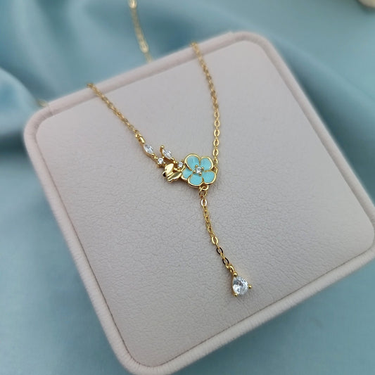 Collar dorado con flor turquesa y gota brillante sobre estuche gris