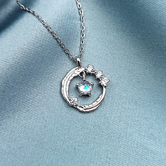 Collar con dije circular plateado y piedra azul en el centro, rodeada de pedrería